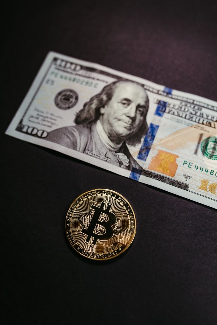 Close-up of a Bitcoin coin with a US 100 dollar bill, symbolizing digital and traditional currency.