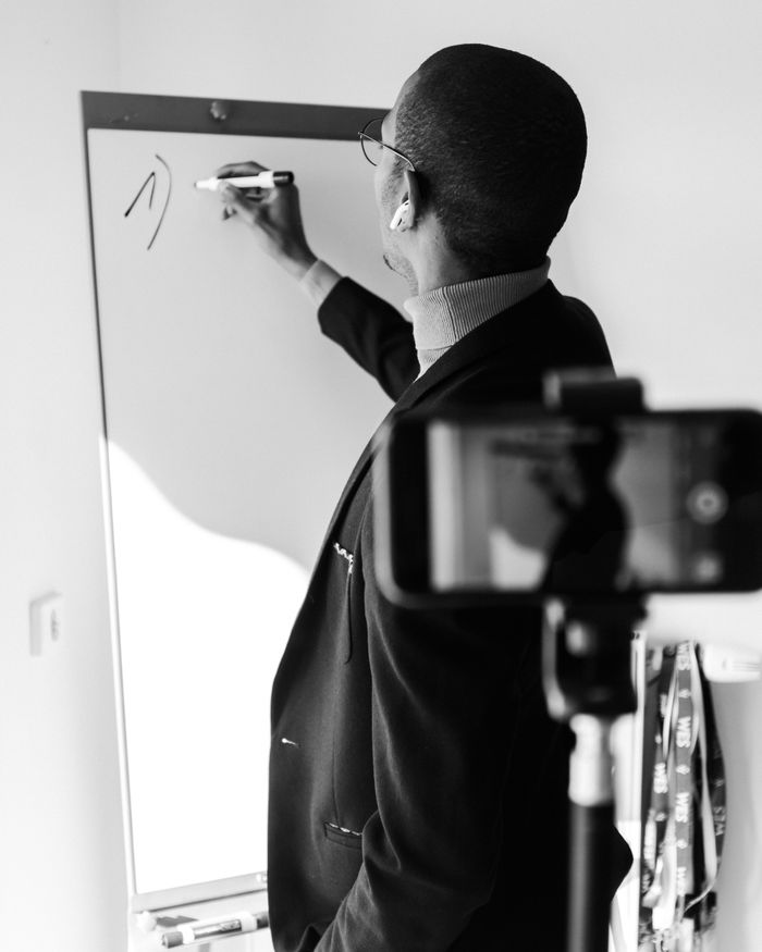 Black and white photo of a professional writing on a whiteboard while being recorded on video, symbolizing modern business presentations.