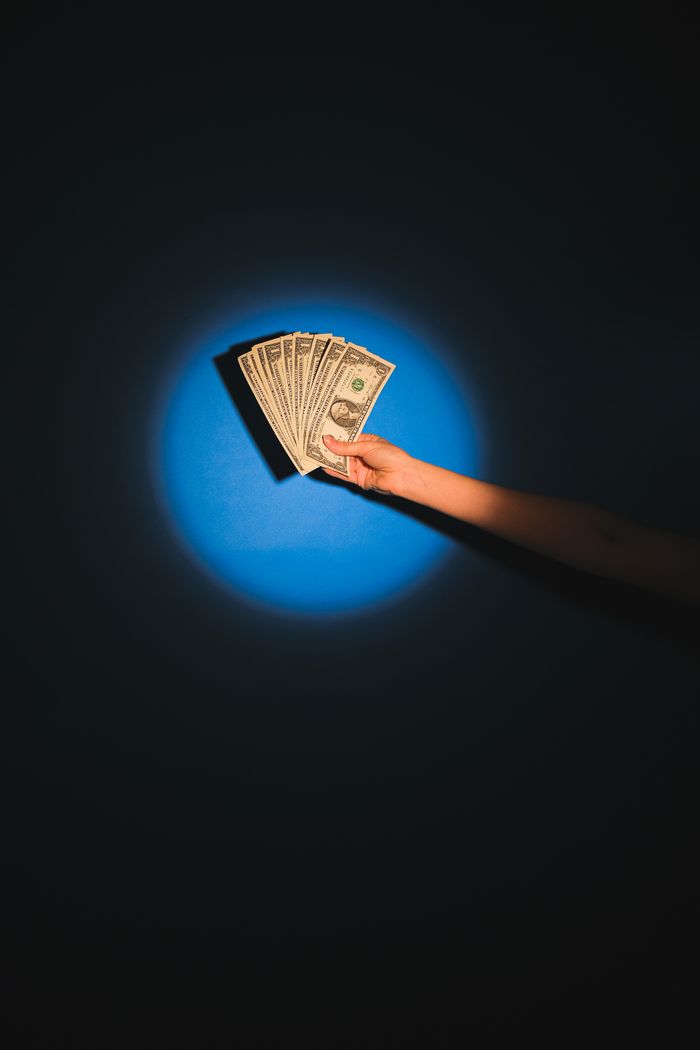 A hand holds fanned out dollar bills against a blue background, symbolizing wealth and finance.