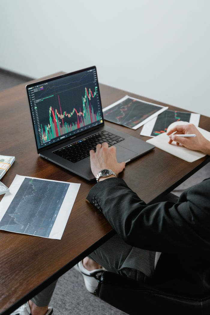 A business analyst reviewing stock charts on a laptop, analyzing market trends.